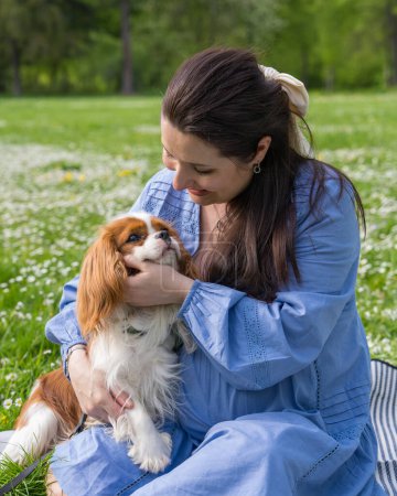 Photo for A pregnant woman in a city park sits on the grass holding a cute cocker spaniel dog in her arms. Love to the animals, - Royalty Free Image
