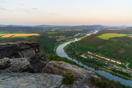 Früh morgens im Nationalpark Sächsische Schweiz. Blick vom hohen Felsen der krummen Elbe auf grüne Felder und Wiesen im Tal. In schönen deutschen Häusern erwacht das Leben