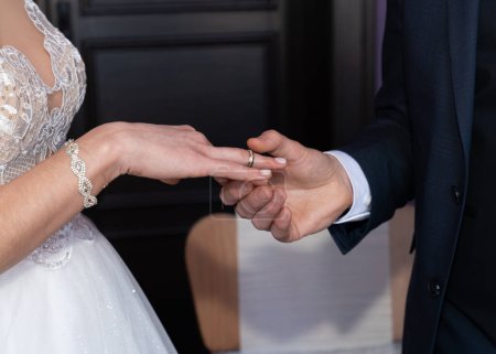The groom puts a wedding ring on the bride's finger. Without a face 