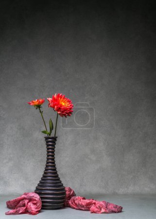 Nature morte avec des dahlias. Deux dahlias rouges dans un vase sombre sur un fond sombre. Espace de copie