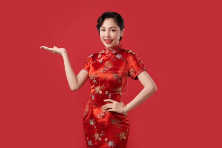 Photo for Happy Chinese new year, Beautiful young Asian woman wearing traditional cheongsam qipao dress with gesture of introduce isolated on red background, - Royalty Free Image