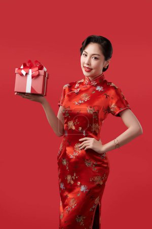 Foto de Feliz año nuevo chino, Hermosa mujer asiática joven con cheongsam tradicional vestido qipao celebración caja de regalo aislado sobre fondo rojo, - Imagen libre de derechos