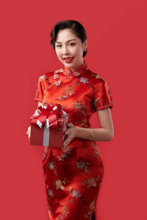 Téléchargez les photos : Happy Chinese new year, Beautiful young Asian woman wearing traditional cheongsam qipao dress holding gift box isolated on red background, - en image libre de droit