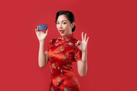Téléchargez les photos : Bonne année chinoise, Belle jeune femme asiatique portant traditionnelle cheongsam qipao robe tenant carte de crédit sur fond rouge, - en image libre de droit
