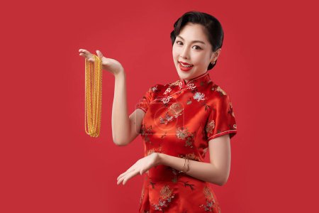 Téléchargez les photos : Nouvel an chinois festival, belle jeune femme asiatique portant traditionnelle cheongsam qipao robe avec des colliers d'or sur fond rouge, - en image libre de droit