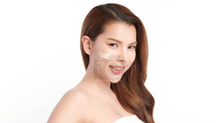Foto de Hermosa mujer asiática joven sonriendo y aplicando crema facial sobre fondo blanco, Cuidado de la piel y rejuvenecimiento, Cuidado de la cara, Tratamiento facial, Cosmetología, belleza, - Imagen libre de derechos
