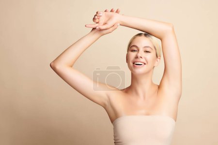 Photo for Beautiful Young woman lifting hands up to show off clean and hygienic armpits or underarms on beige background, Smooth armpit cleanliness and protection concept - Royalty Free Image