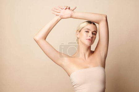 Téléchargez les photos : Belle jeune femme levant les mains pour montrer des aisselles ou aisselles propres et hygiéniques sur fond beige, concept de propreté et de protection des aisselles lisses - en image libre de droit