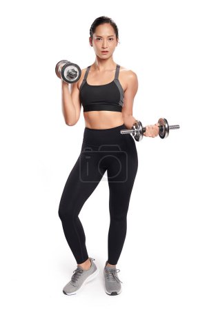 Photo for An asian woman is working out with dumbbells wearing the sport exercise suit with white background, - Royalty Free Image