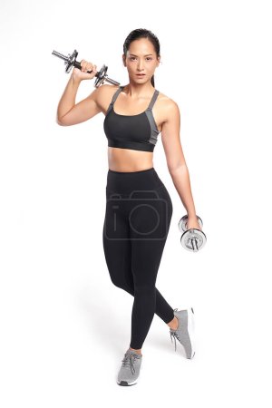 Photo for An asian woman is working out with dumbbells wearing the sport exercise suit with white background, - Royalty Free Image