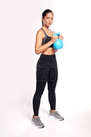 Foto de Una mujer asiática está haciendo ejercicio con kettlebell usando el traje de ejercicio deportivo con fondo blanco, - Imagen libre de derechos