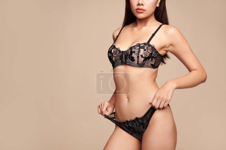 Foto de Confiado hermosa joven mujer asiática posando en lencería negra sobre fondo beige, Cuerpo perfecto, - Imagen libre de derechos