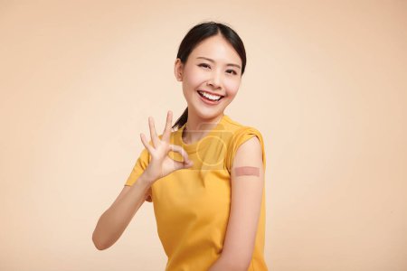 Saludable mujer asiática recibiendo inmunidad vacunada dando señal de mano ok en fondo beige, concepto de inoculación recomendada, vacunación, 