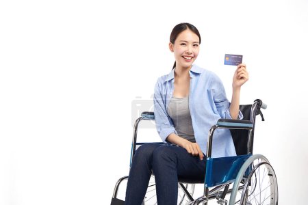 Téléchargez les photos : Jeunes femmes asiatiques avec sourire heureux et montrer carte de crédit assis dans un fauteuil roulant sur fond blanc, concept de soins de santé, accident, assurance, assurance vie, bien-être, hôpital. - en image libre de droit
