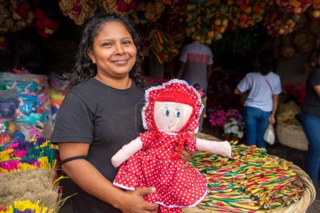 Téléchargez les photos : Jeune femme latine vendant de l'artisanat dans le marché Masaya au Nicaragua tenant une poupée en chiffon dans ses mains - en image libre de droit