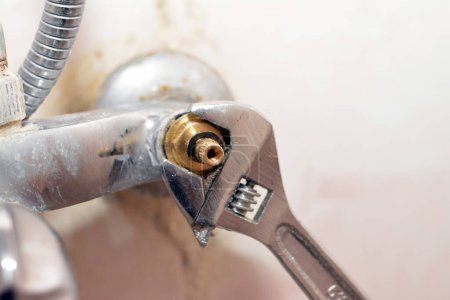 A plumber fixing a problem of a shower faucet tap spinning the cartridge body with an adjustable wrench tool to change it, plumbing and maintenance concept background at home, selective focus