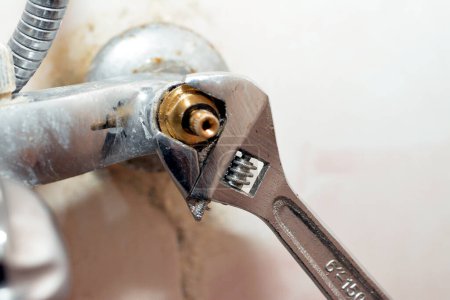 Photo for A plumber fixing a problem of a shower faucet tap spinning the cartridge body with an adjustable wrench tool to change it, plumbing and maintenance concept background at home, selective focus - Royalty Free Image