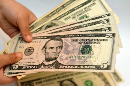 Téléchargez les photos : Cinq billets de 5 dollars américains dans la main d'un jeune enfant représente le portrait d'Abraham Lincoln, le 16e président des États-Unis, concept d'avenir économique et financier - en image libre de droit