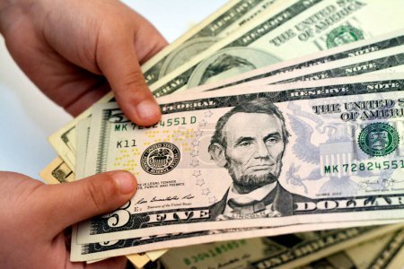 Téléchargez les photos : Cinq billets de 5 dollars américains dans la main d'un jeune enfant représente le portrait d'Abraham Lincoln, le 16e président des États-Unis, concept d'avenir économique et financier - en image libre de droit