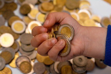 Téléchargez les photos : Un tas de pièces dans la main d'un enfant, pile de pièces d'argent égyptiennes détenues par un jeune enfant, le concept d'avenir de l'économie, la collecte d'argent pour la charité, et économiser de l'argent - en image libre de droit