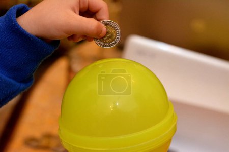 Photo for A young child putting a coin in a plastic child saving bank, concept of saving money and collecting money for charity, selective focus of Egyptian money coins in a child's hand - Royalty Free Image