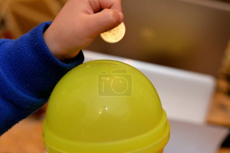 Foto de Un niño pequeño poniendo una moneda en un banco de ahorro de plástico, concepto de ahorrar dinero y recoger dinero para la caridad, enfoque selectivo de monedas de dinero egipcio en la mano de un niño - Imagen libre de derechos