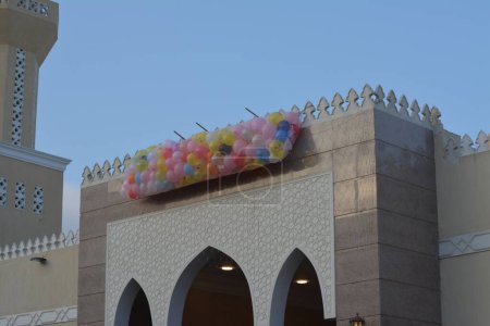 Téléchargez les photos : Contexte des festivités et des célébrations devant une mosquée au Caire Egypte avec des dizaines de ballons détenus sur le toit de la mosquée à côté du minaret à jeter et à libérer pour les enfants après la prière de fête de l'Aïd - en image libre de droit