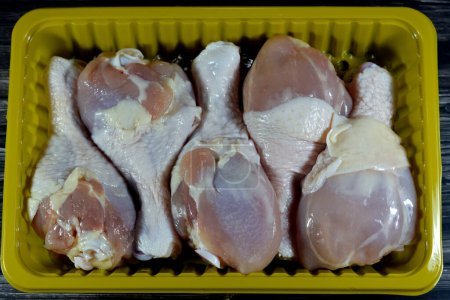 Photo for Fresh raw chicken legs drumsticks hindquarter with skin and bones that is ready for baking, grilling, barbecuing, frying or boiling, selective focus of white meat of chicken legs in yellow plate - Royalty Free Image