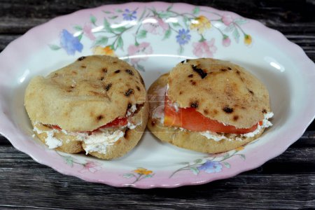 Photo for Feta white cheese with slices of tomatoes inside a mini traditional Egyptian flat bread with wheat bran and flour, small Aish Baladi or small bread baked in extremely hot ovens, breakfast snack - Royalty Free Image