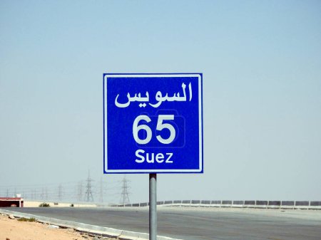 Téléchargez les photos : Un panneau de signalisation à Suez autoroute du Caire donne la distance restante à la ville de Suez 65 KM soixante-cinq kilomètres écrits en anglais et le mot Suez écrit en arabe et en anglais sur le côté de la rue - en image libre de droit