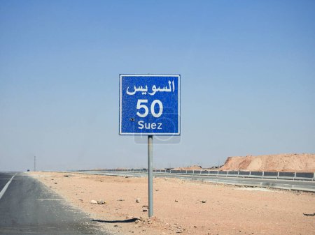 Téléchargez les photos : Un panneau de signalisation à Suez autoroute du Caire donne la distance restante à la ville de Suez 50 KM cinquante kilomètres écrits en anglais et mot Suez écrit en arabe et en anglais sur le côté de la rue - en image libre de droit