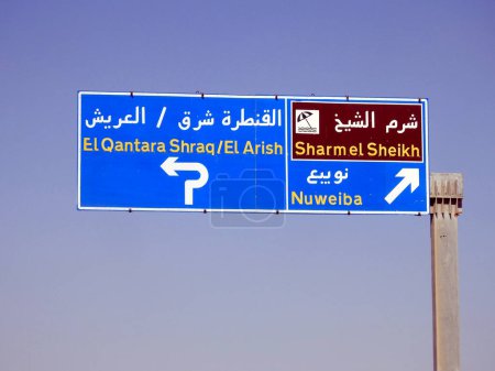 Foto de Una señal de tráfico lateral direccional tablero informativo en el sur del Sinaí da direcciones de Sharm El Sheikh, Qantara Oriental, Arish y Nuweiba ciudades en la carretera escrita en árabe e inglés - Imagen libre de derechos