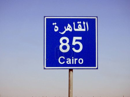 Téléchargez les photos : Un panneau de signalisation à Suez autoroute du Caire donne la distance restante à la ville du Caire 85 KM quatre-vingt-cinq kilomètres écrits en mots anglais et arabe sur le côté de la rue près du Caire - en image libre de droit
