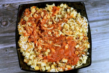 Photo for Egyptian cuisine of Koshary, a popular street food made of rice, macaroni, spaghetti and lentils mixed together topped with a spiced tomato sauce, garlic vinegar, fried onions and hummus chickpeas - Royalty Free Image