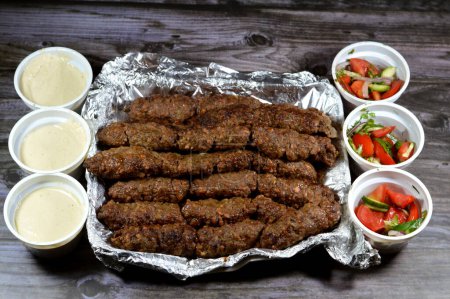 Photo for Arabic cuisine traditional food beef Kofta, kebab and tarb kofta shish, minced meat wrapped in lamb fat charcoal grilled, with green and Tahini salad, oriental grilled barbecued meat food - Royalty Free Image