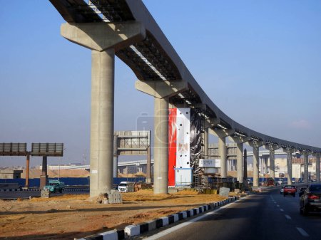 Foto de El Cairo, Egipto, 7 de octubre de 2023: sitio de monorraíl de El Cairo que está en construcción por la compañía Orascom con las columnas y las vías, sistema de tránsito rápido, con la bandera egipcia en él, enfoque selectivo - Imagen libre de derechos