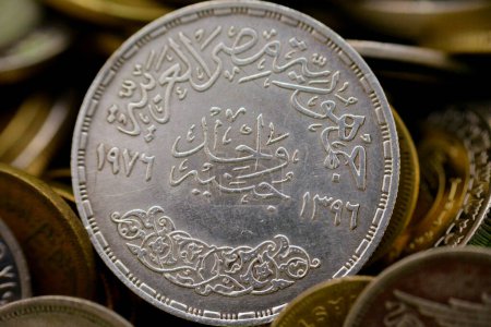Photo for The reverse side of Egyptian one pound coin, 1 LE silver coin year 1976 AD, 1396 AH with a Commemoration slogan of Saudi King Faisal bin Abdulaziz on the obverse side on a blurred coins background - Royalty Free Image