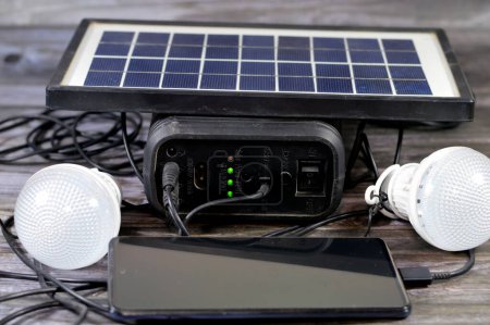 Foto de Una batería multipropósito cargada con un panel solar, un dispositivo que convierte la luz solar en electricidad mediante el uso de células fotovoltaicas (PV), con el teléfono celular de carga a través del puerto USB y la luz led conectada - Imagen libre de derechos