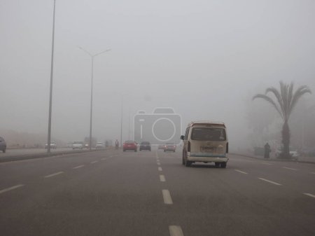 Téléchargez les photos : Le Caire (Égypte), le 31 décembre 2023 : mauvaise visibilité sur une route en Egypte tôt le matin, prévisions météorologiques de brouillard, brouillard ou brume, conduite dangereuse, état de la circulation - en image libre de droit