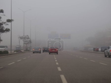 Téléchargez les photos : Le Caire (Égypte), le 31 décembre 2023 : mauvaise visibilité sur une route en Egypte tôt le matin, prévisions météorologiques de brouillard, brouillard ou brume, conduite dangereuse, état de la circulation - en image libre de droit