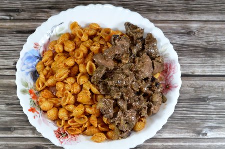 tasty appetizing classic pasta shell macaroni plate with tomato sauce, garlic, onion, spices, oil and black pepper with Grilled chicken livers and hearts sliced in pieces cooked with oil