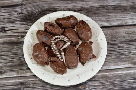 Silberner Rosenkranz und mit Schokolade überzogene Datteln sorgen für den besten Snack, Leckerbissen oder Dessert, schmackhafte saudische Datteln, die mit brauner Schokolade überzogen sind, Datteln, die normalerweise im Ramadan-Monat in islamischen Ländern verzehrt werden