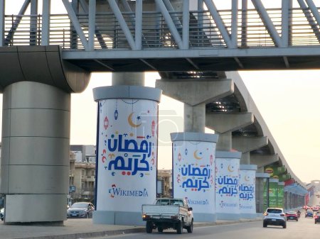 Foto de El Cairo, Egipto, 29 de marzo de 2024: Ramadán Kareem Feliz mes de Ramadán generoso escrito en árabe en las columnas de monorraíl de El Cairo, Egipto que está en construcción, sistema de tránsito rápido, nuevo proyecto inmobiliario - Imagen libre de derechos