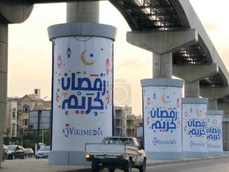Foto de El Cairo, Egipto, 29 de marzo de 2024: Ramadán Kareem Feliz mes de Ramadán generoso escrito en árabe en las columnas de monorraíl de El Cairo, Egipto que está en construcción, sistema de tránsito rápido, nuevo proyecto inmobiliario - Imagen libre de derechos