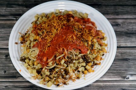 Egyptian cuisine of Koshary, a popular street food made of rice, macaroni, spaghetti and lentils mixed together topped with a spiced tomato sauce, garlic vinegar, fried onions and hummus chickpeas