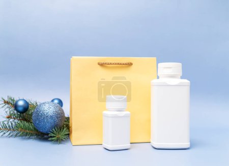 Weihnachts-Apotheke zwei weiße Pillen-Flaschen, goldenes Papier-Paket, Weihnachtsbaum, funkelnde Spielzeugkugeln auf blauem Hintergrund. Winterurlaub, medizinisches Konzept. Horizontale Ebene