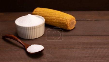 Bio-Süßstoff kalorienfreies Erythrit, hergestellt durch Fermentation aus Mais, Dextrose genannt in Keramikschüssel, Holzlöffel, Maiskolben auf braunem Holztisch. Zuckerersatz.Horizontale Ebene, Kopierraum