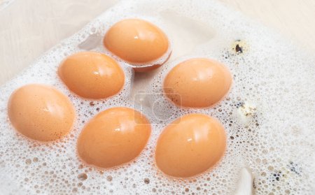 Photo for Chicken and quail eggs in soapy soda water in container. Hygiene, cleaning, washing products as disease prevention, salmonella. Top view, nobody. Horizontal plane. High quality photo. - Royalty Free Image