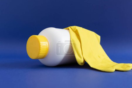 Photo for Pipe Unclogging Granules In Yellow Cap, White Plastic Bottle, Rubber Glove On Blue Purple Background. Super Drain Cleaner, Housework Help. Horizontal Plane, Closeup. High quality photo - Royalty Free Image