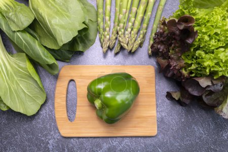 Photo for Top View Assortment Of Fresh Organic Vegetables, Green Bell Pepper On Cutting Board On Table. Asparagus Plant, Bok Choy, Red Leaf Lettuce. Healthy Bio Food. Horizontal Plane. Flatly - Royalty Free Image